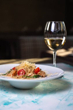 Sert peynirli makarna ve arkasında şarap olan et.