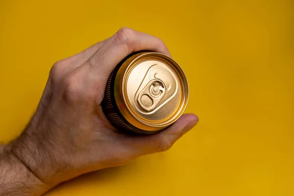 metal beer can in a man\'s hand on a yellow background.