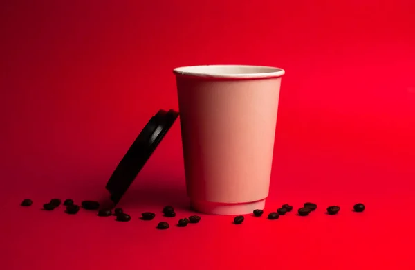 Copo de papel aberto de café com grãos em um fundo vermelho — Fotografia de Stock
