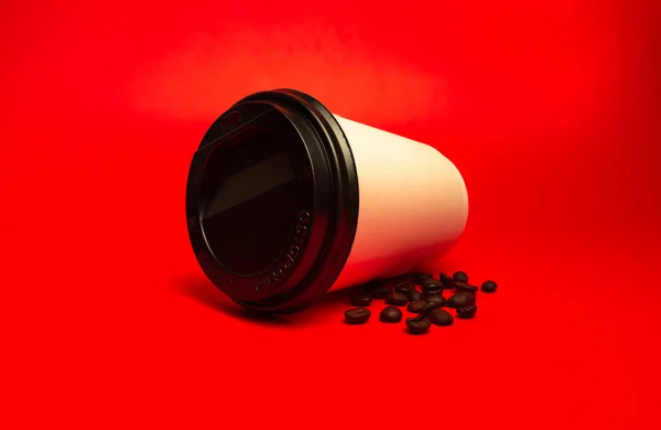 Copo de papel branco com grãos de café em um fundo vermelho — Fotografia de Stock