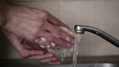 Bir adam musluğun altında cam bardak yıkıyor.