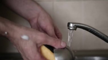 Bir adam musluğun altında bulaşık yıkar.