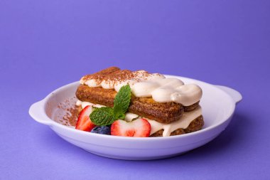 Tiramisu in a white bowl: layers of biscuit, cream, cocoa powder, garnished with strawberries, blueberries, and mint. Perfect for patisseries, summer menus, or coffee shop promotions 