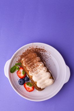Tiramisu in white bowl: layers of biscuit, cream, cocoa powder, garnished with strawberries, blueberries, and mint leaf. Perfect for patisseries, summer menus, or coffee shop promotions