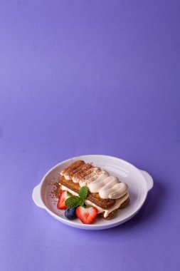 Tiramisu in a white bowl: layers of biscuit, cream, cocoa powder, garnished with strawberries, blueberries, and mint. Perfect for patisseries, summer menus, or coffee shop promotions 