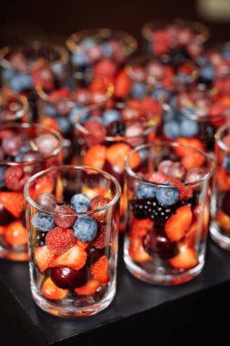 Şeffaf bardaklarda canlı çilekler, yaban mersinleri, böğürtlenler ve kirazlar. Lüks yemek, düğün tasarımı ya da sağlık kampanyaları için ideal