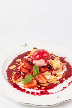 Bir dilim çilekli turtayı yakın plan beyaz arka planda bir kepçe dondurma ve badem gevreğiyle servis et..