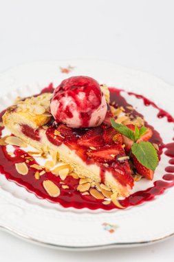 Dondurma kepçeli zarif çilekli tart, badem gevreği ve beyaz tabakta nane yaprakları, menüler ya da reklamlar için mükemmel..