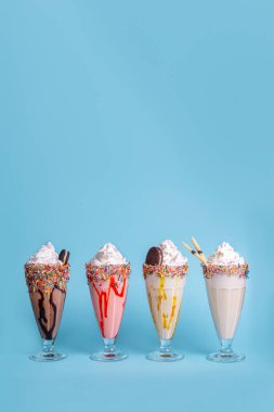 Mavi arka planda gözlüklerle servis edilen renkli milkshake 'ler yaz için mükemmel tatlı içecekler, menü tasarımı ve yemek reklamı..