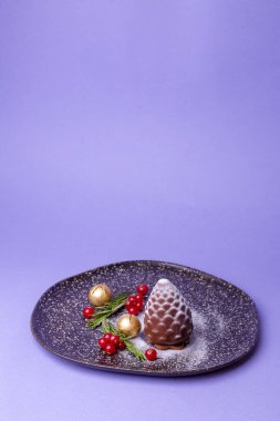 Kırmızı böğürtlenli çam kozalağı şeklindeki çikolatalı tatlı ve siyah tabakta altın süsler..