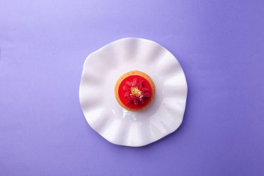 Beyaz tabakta ahududu ve altın kaplamalı tatlı, mor arkaplanda minimalist tatlı estetik..