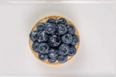 Yaban mersinli mini tart manzarası, beyaz arka planda taze yaz tatlılığı.