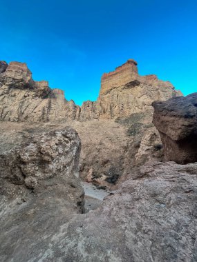 Charyn Kanyonu kaya oluşumlarının alçak açılı görüntüsü: engebeli taş dokusu ve mavi gökyüzüne karşı kale benzeri zirveler.