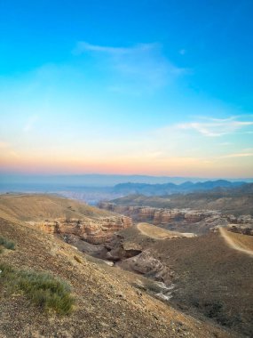 Gün batımında kanyon manzarası: kumlu tepeler, kıvrımlı yollar ve pembe-turuncu ufuk..