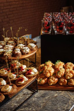 Aperatifler, kruvasanlar ve mermer tezgahta duran tuğla duvar arkası, düğün resepsiyonları ve lüks etkinlik planlama için ideal olan dut bardaklarıyla zarif bir yemek düzenleme..