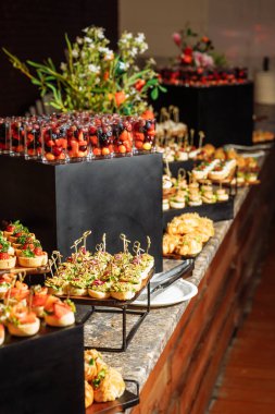 Canlı böğürtlen içeren şık yemek masası - shot bardakları, çeşitli mini tartlar ve siyah basamaklarda gurme kanepeler