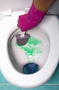 Pembe kauçuk eldivenli biri, beyaz klozetin içine yeşil köpük temizleyiciyle gri silikon tuvalet fırçası sürüyor. Hijyenik banyo temizliği, ev işi ve modern hijyen aletleri iş başında..