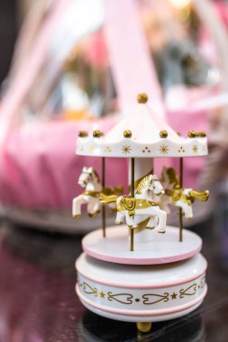 Altın atlar, yıldızlar ve süslü detaylarla dolu hassas pembe ve beyaz bir atlıkarınca müzik kutusuna odaklanın. Yumuşak pembe arka planlı lüks bir bebek hediyesi yerleştirin.