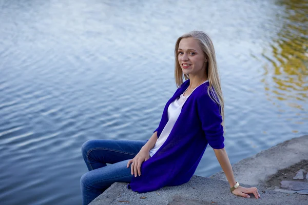 Blond dívka sedící s nohama visící nad vodou — Stock fotografie