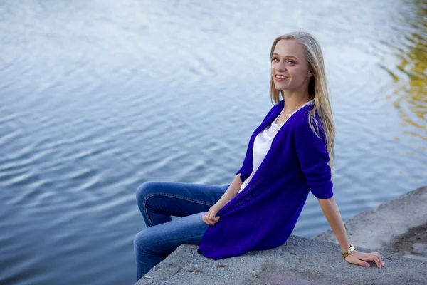 Blond dívka sedící s nohama visící nad vodou — Stock fotografie