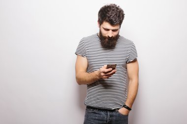 Beyaz izole arka plan üzerinde duran ve cep telefonu tutan sakallı gülümseyen adam.