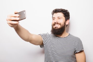 Beyaz izole arka plan üzerinde duran ve cep telefonu ile selfie çekerken sakallı portre gülümseyen adam.