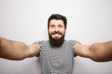 Beyaz izole arka plan üzerinde duran ve kamera elleri ile selfie çekerek sakallı mutlu gülümseyen hipster adam.