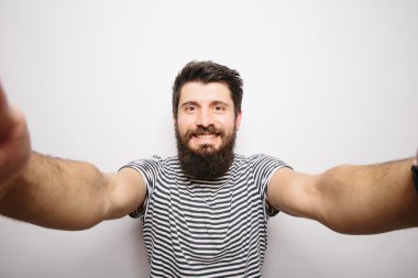 Beyaz izole arka plan üzerinde duran ve kamera elleri ile selfie çekerek sakallı mutlu gülümseyen hipster adam.
