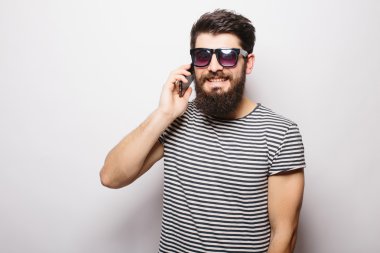 Beyaz arka plan aleyhine telefonda konuşurken güneş gözlüğü sakallı yakışıklı mutlu adam