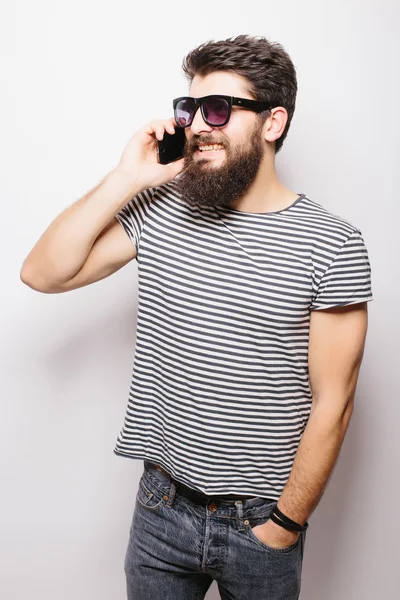 Hombre feliz guapo con barba en gafas de sol hablando por teléfono sobre fondo blanco — Foto de Stock