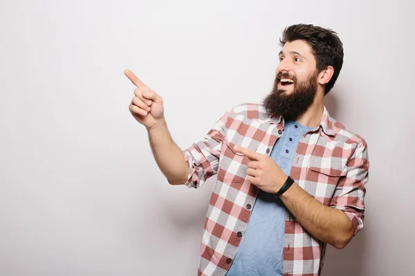 Jovem bonito com barba demonstrar apresentação do produto invisível ou publicidade apontada com as mãos enquanto em pé contra fundo branco — Fotografia de Stock