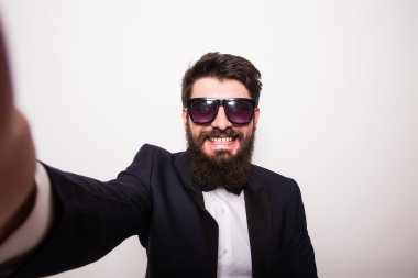 siyah takım elbise ve güneş gözlüğü yakışıklı genç adam selfie yapma ve gri arka plan karşı dururken gülümseyerek