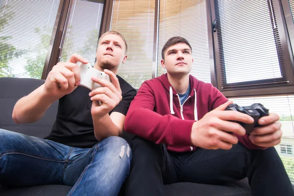 Deux beaux jeunes hommes jouant à des jeux vidéo assis sur le canapé — Photo