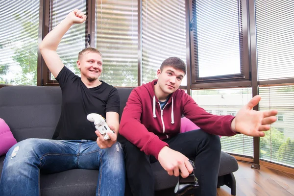 Двоє красивих молодих чоловіків грають у відеоігри, сидячи на дивані — стокове фото