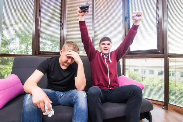 Two handsome young men playing video games while sitting on sofa — Stock Photo, Image