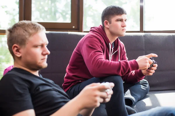 Δύο νεαροί άνδρες παίζουν βιντεοπαιχνίδια ενώ κάθεται στον καναπέ — Φωτογραφία Αρχείου