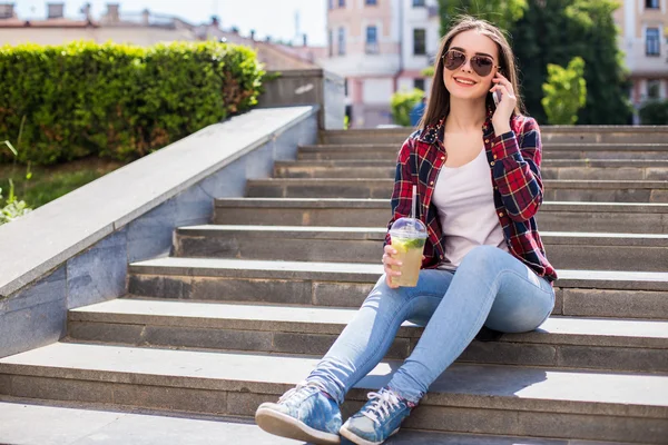 Mujer con una taza fresca sentada en las escaleras y usando su smartphone para comunicarse . — Foto de Stock