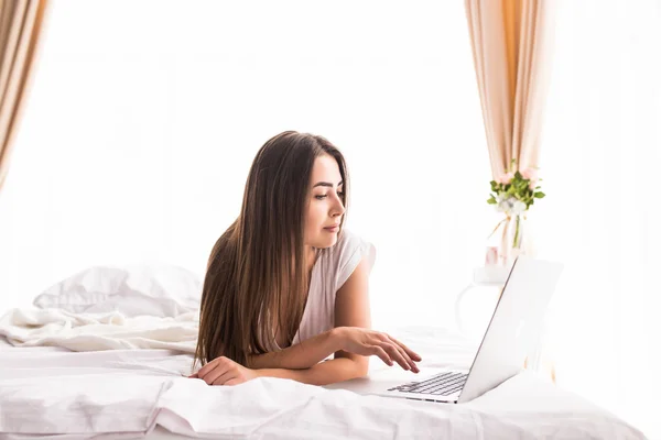 Chica bonita mirando el monitor del ordenador portátil mientras está acostado en la cama en su habitación — Foto de Stock