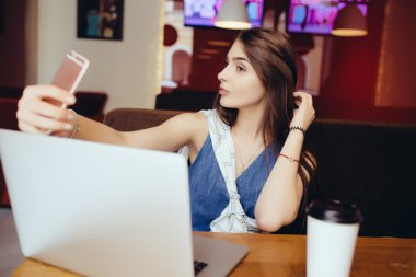  kafede selfie ve dizüstü bilgisayar almak için bir akıllı telefon kullanan kız