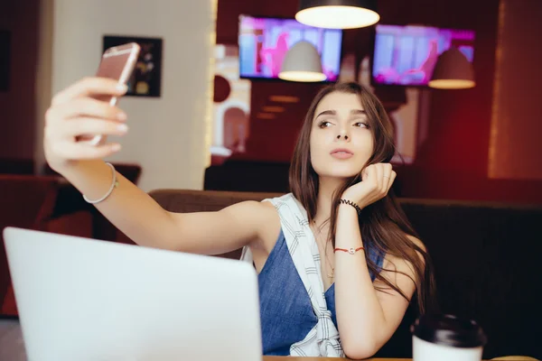 Girl using a smart phone to take selfie and laptop computer in cafe — Stock Photo, Image