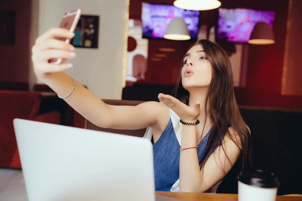 Girl using a smart phone to take selfie and laptop computer in cafe — Stock Photo, Image