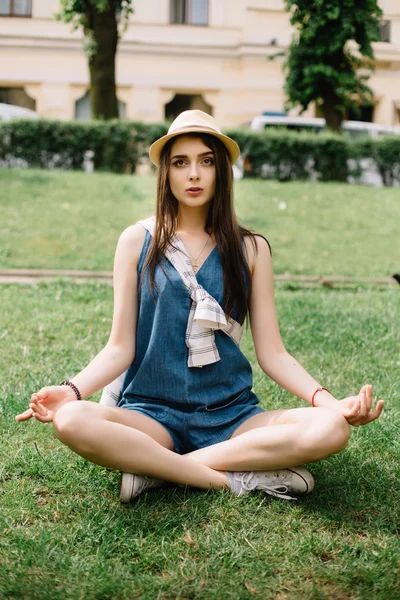 Girl sitting on grass with crossed legs in city square. — Stock Photo, Image