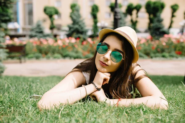 Menina com óculos de sol deitado na grama no dia de verão no parque da cidade . — Fotografia de Stock