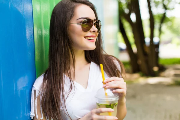 Mujer con copa de bebida en gafas de sol y sombrero sobre fondo de color — Foto de Stock
