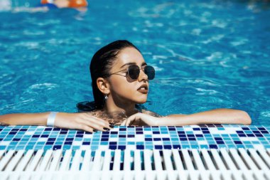 Beyaz bikinili, bronzlaşmış ince vücutlu zarif seksi kadın yüzme havuzunun yanında poz veriyor.