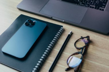 Telefon, gözlük, günlük ve kalem ahşap masa manzarasında.