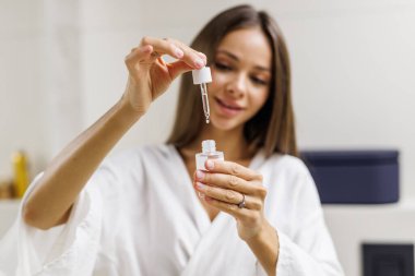 Güzel bir kadın banyoda yüzüne yaşlanma önleyici serum tedavisi uyguluyor..