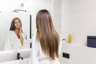 Çekici bir kadın güzel yüzüne dokunuyor ve banyoda dururken gülümsüyor.