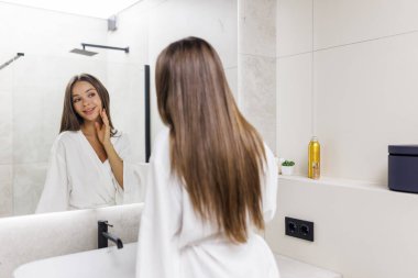 güzel gülümseyen yüzünü dokunaklı ve banyo aynaya bakarak genç kadın