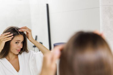 Woman controls hair loss and unhappy gazing at you in the mirror
